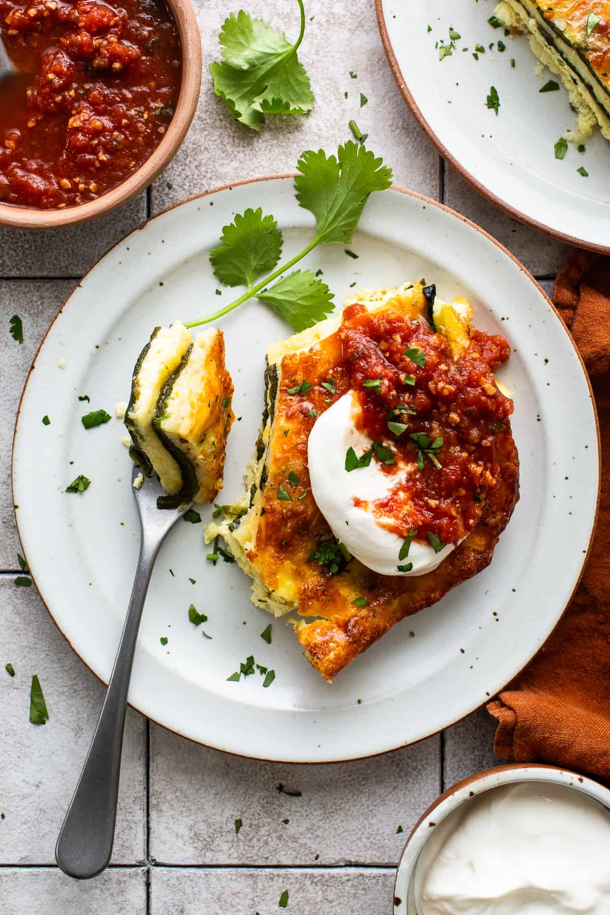 A slice of chile relleno casserole served with sour cream and salsa.