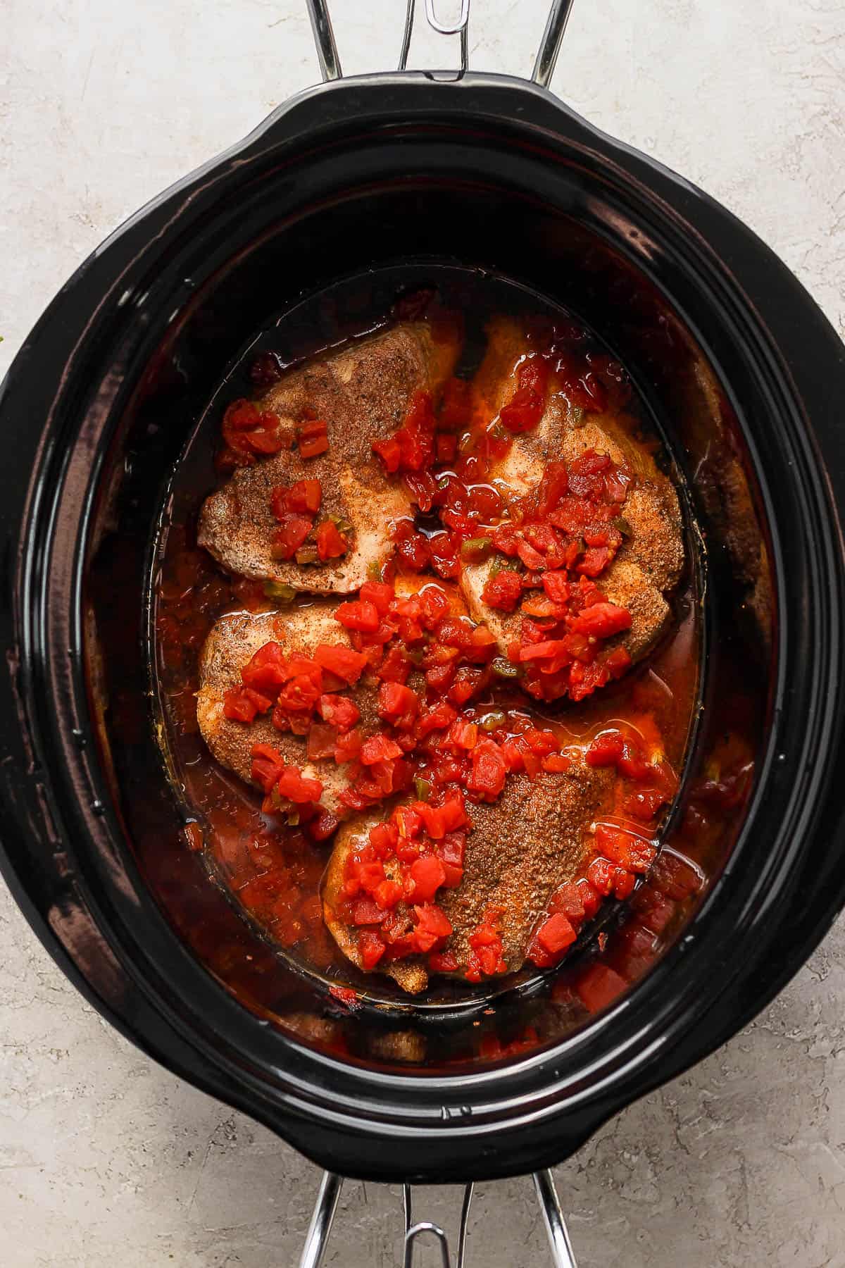 Seasoned chicken breast topped with diced tomatoes and green chiles in a slow cooker.