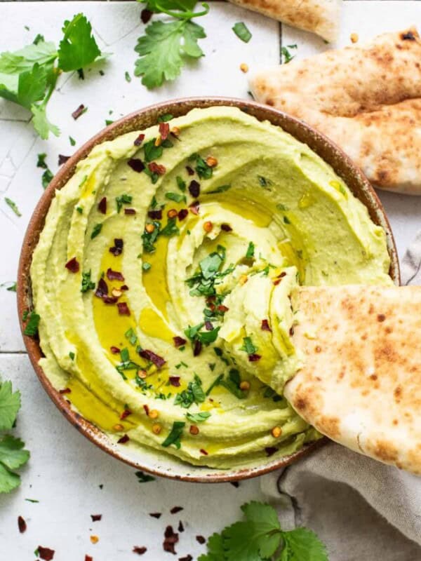 A slice of pita bread being dipped in a bowl of avocado hummus.