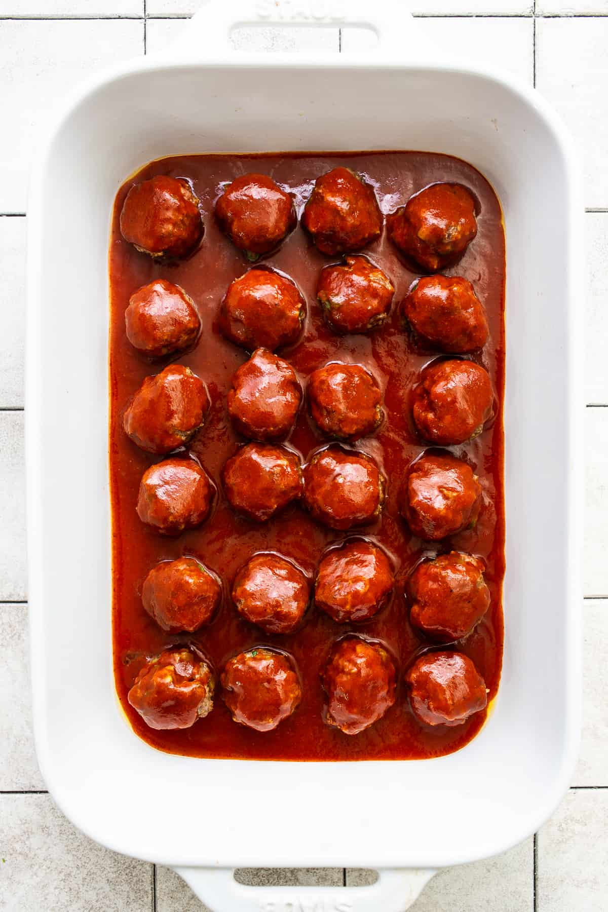 Enchilada sauce poured on top of meatballs in a baking dish.