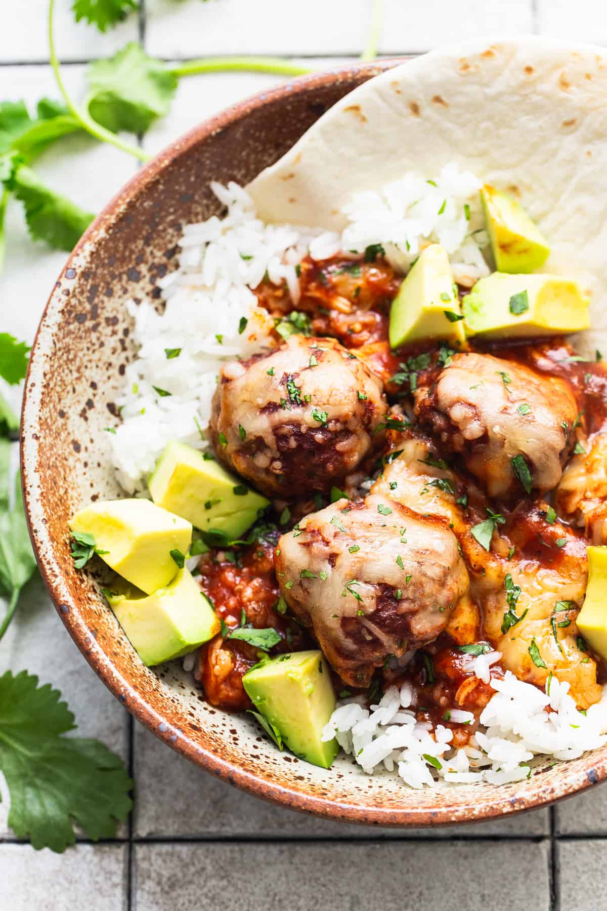 Enchilada meatballs in a bowl with white rice and garnished with diced avocado.