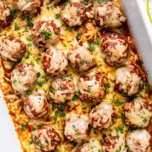 Enchilada meatballs baked in dish topped with cheese, cilantro, and enchilada sauce.