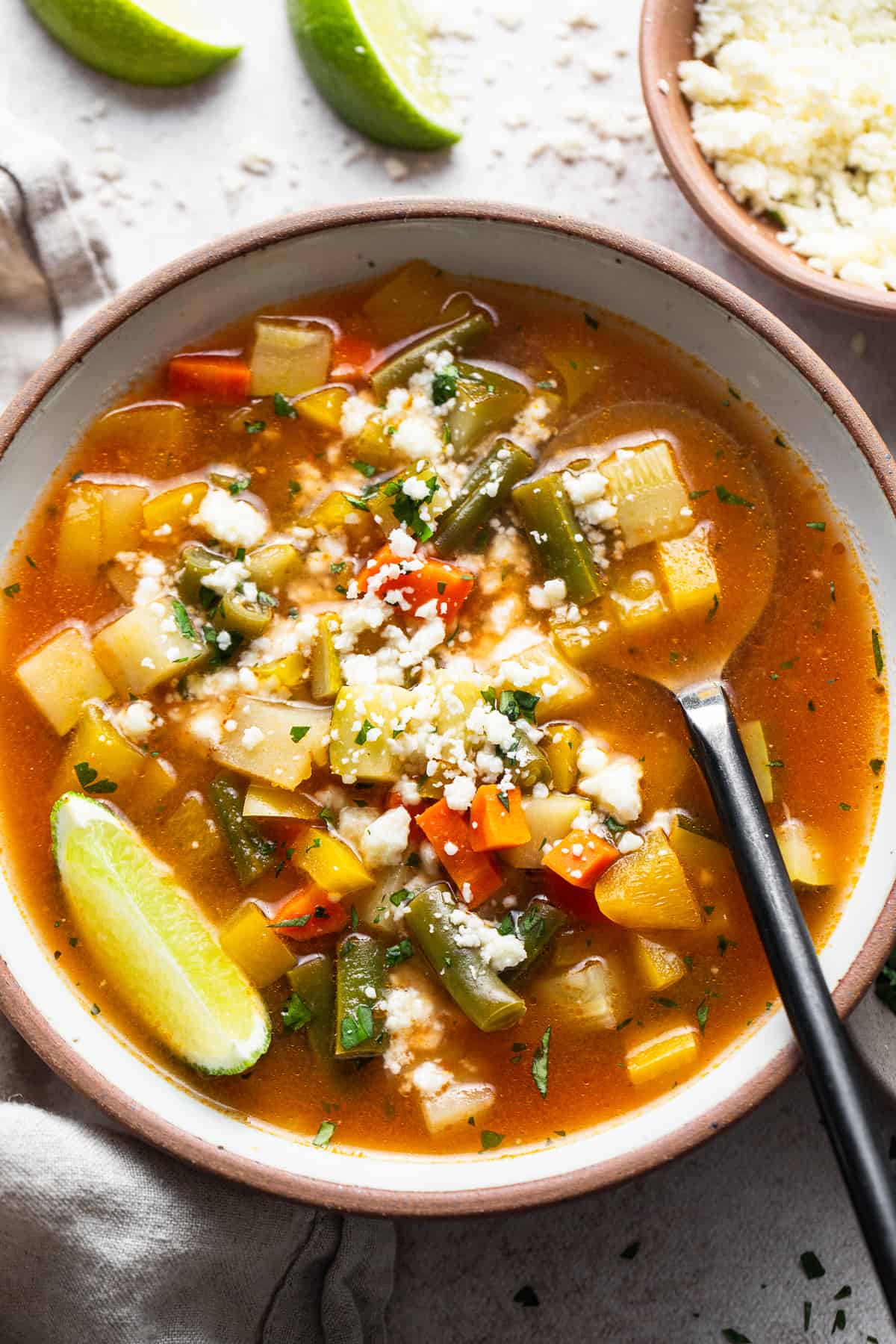 Mexican Vegetable Soup in a bowl garnished with lime juice and cotija cheese.