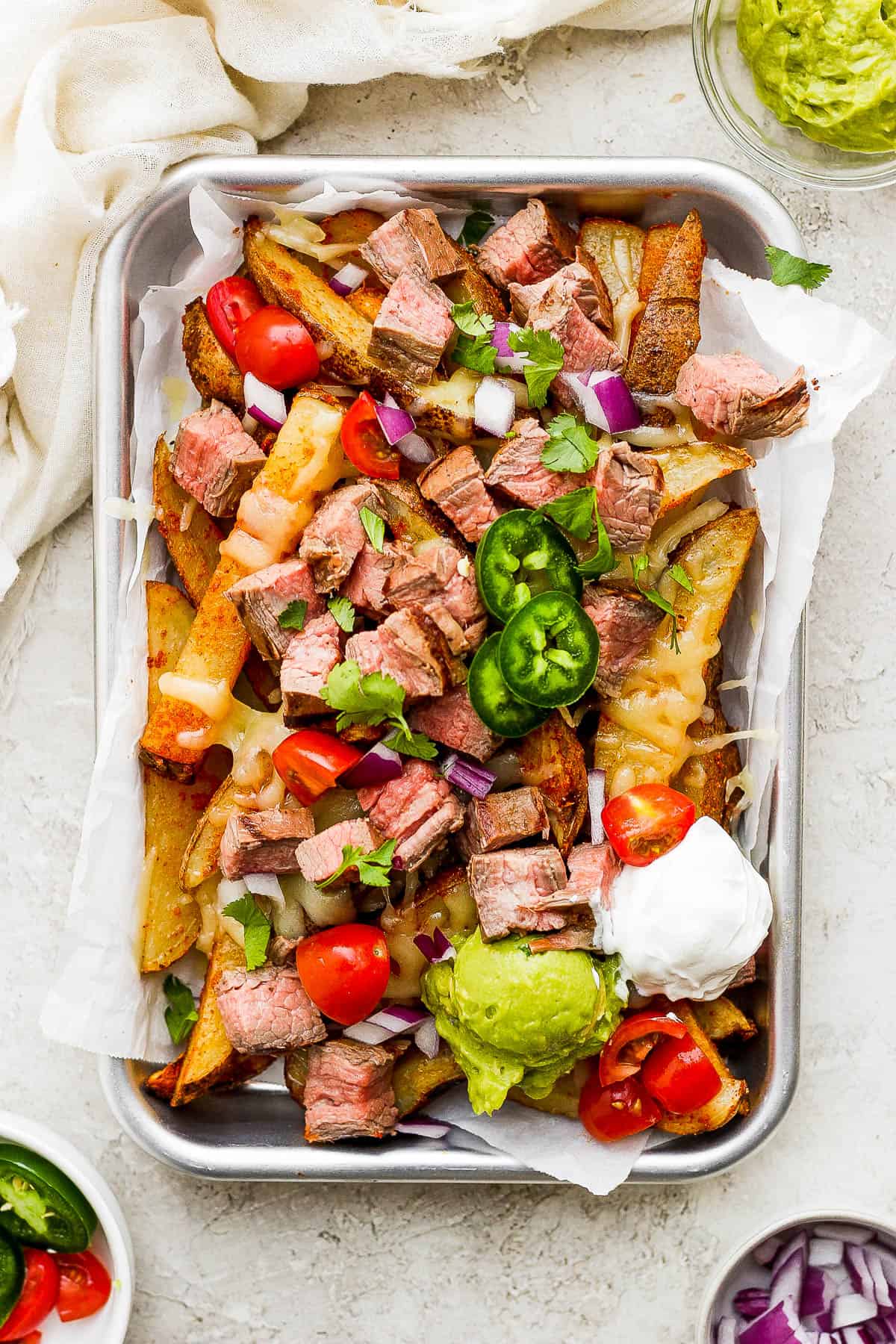 A plate of carne asada fries served with a dollop of sour cream and guacamole.