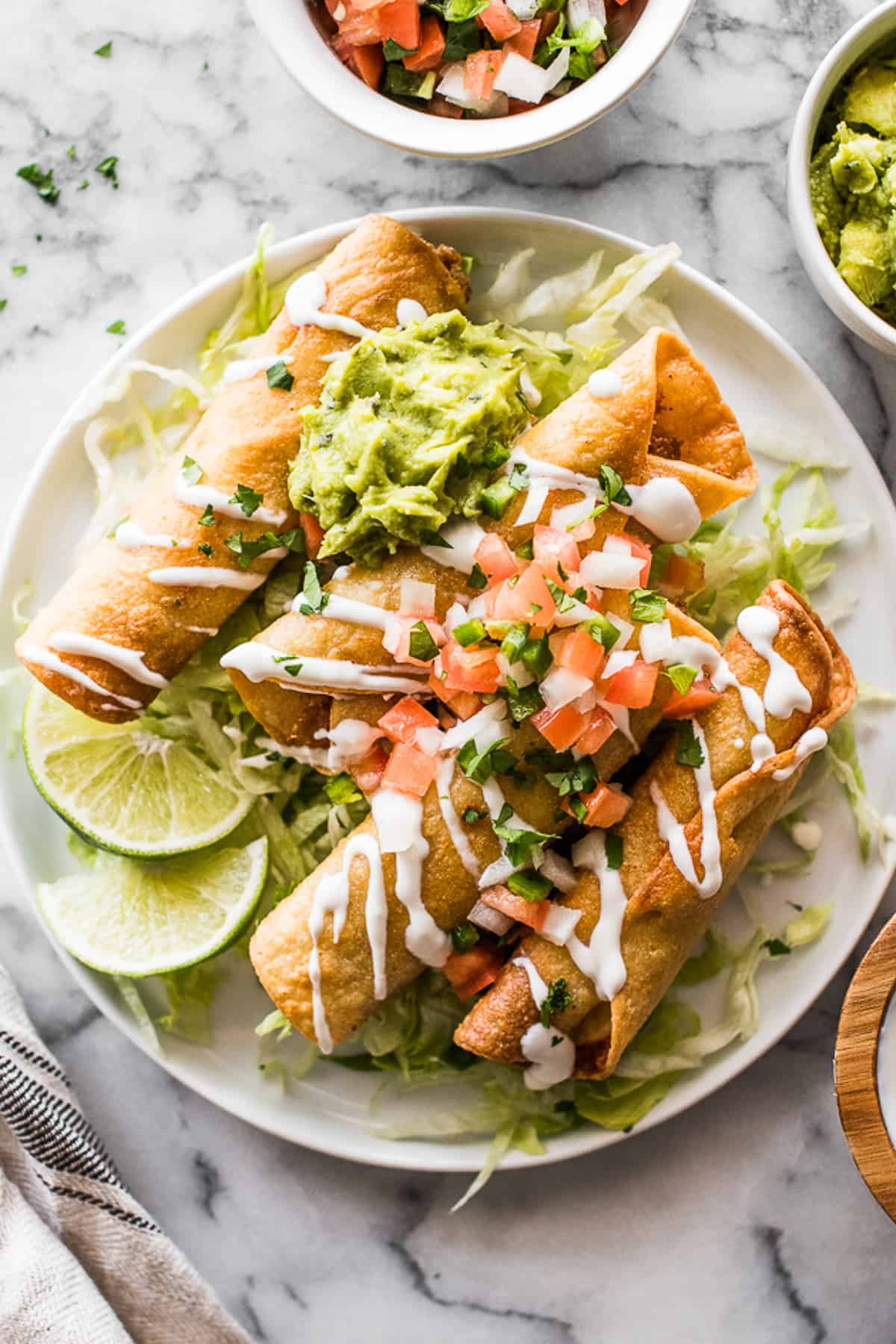 Chicken taquitos on a plate topped with guacamole and pico de gallo.