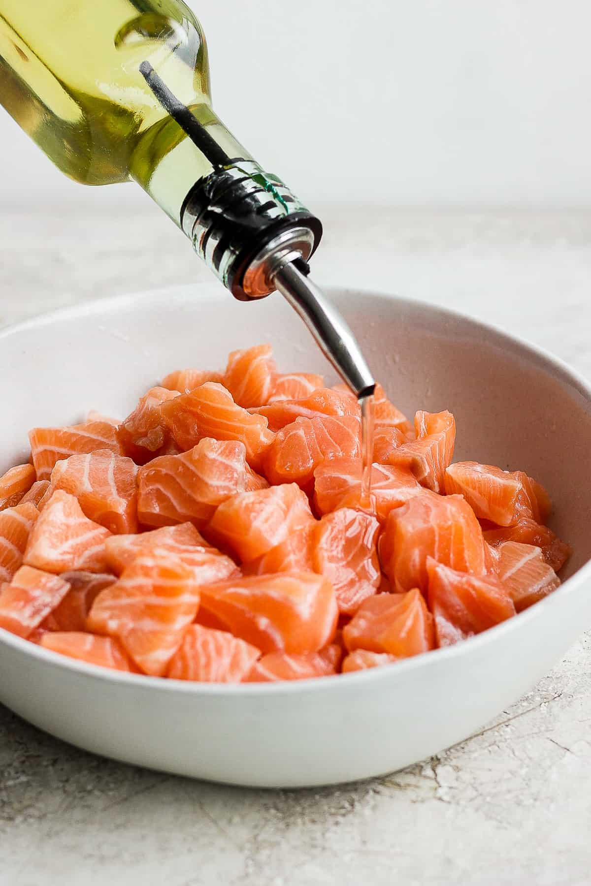 Oil being poured into a bowl of salmon bites.