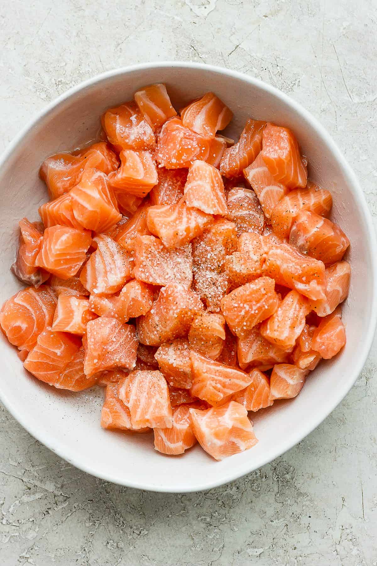 Salmon bites in a bowl seasoned with kosher salt, black pepper, and tossed in oil.