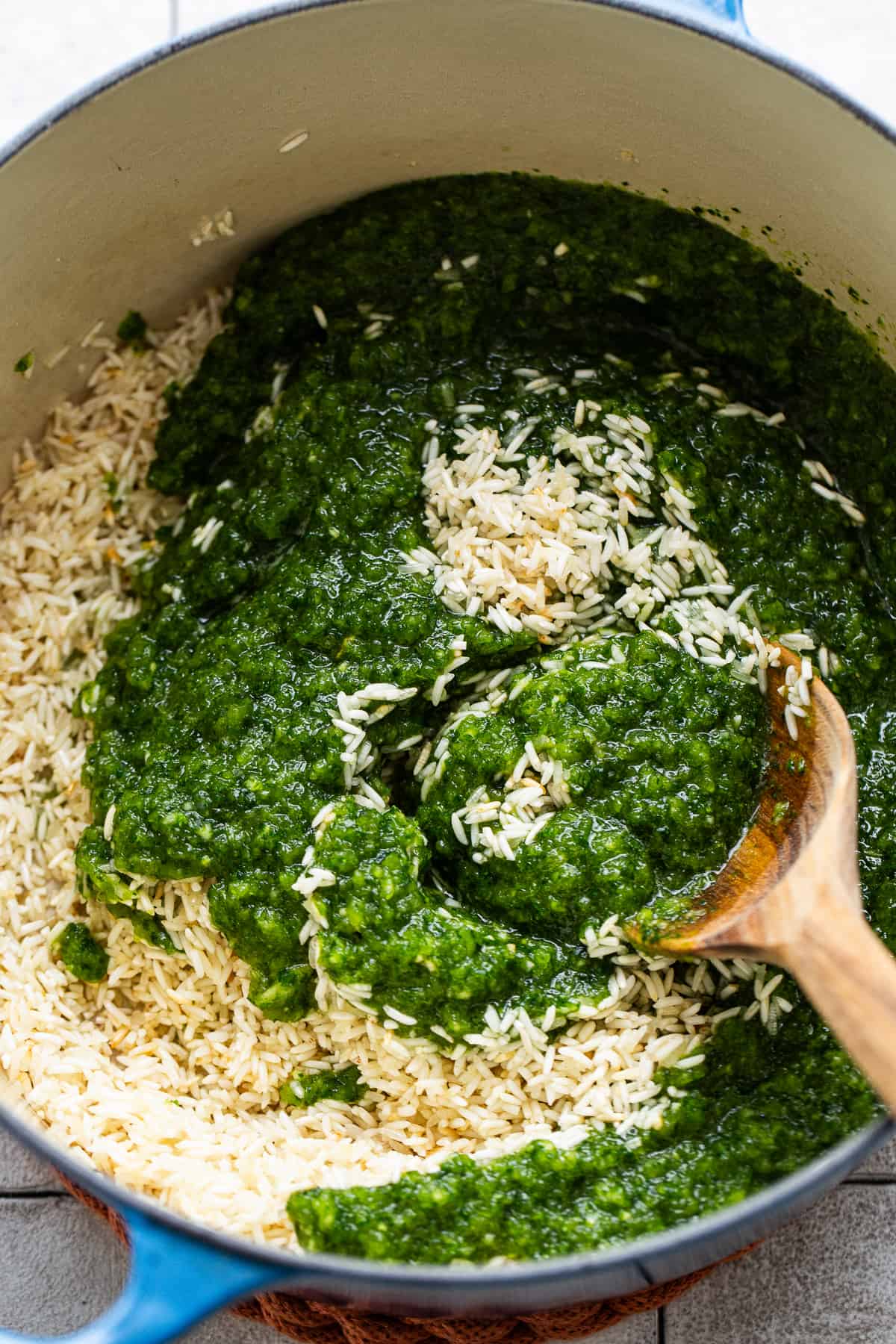 A verde mixture made of blended herbs, peppers, and onions being stirring into a pot of toasted rice.