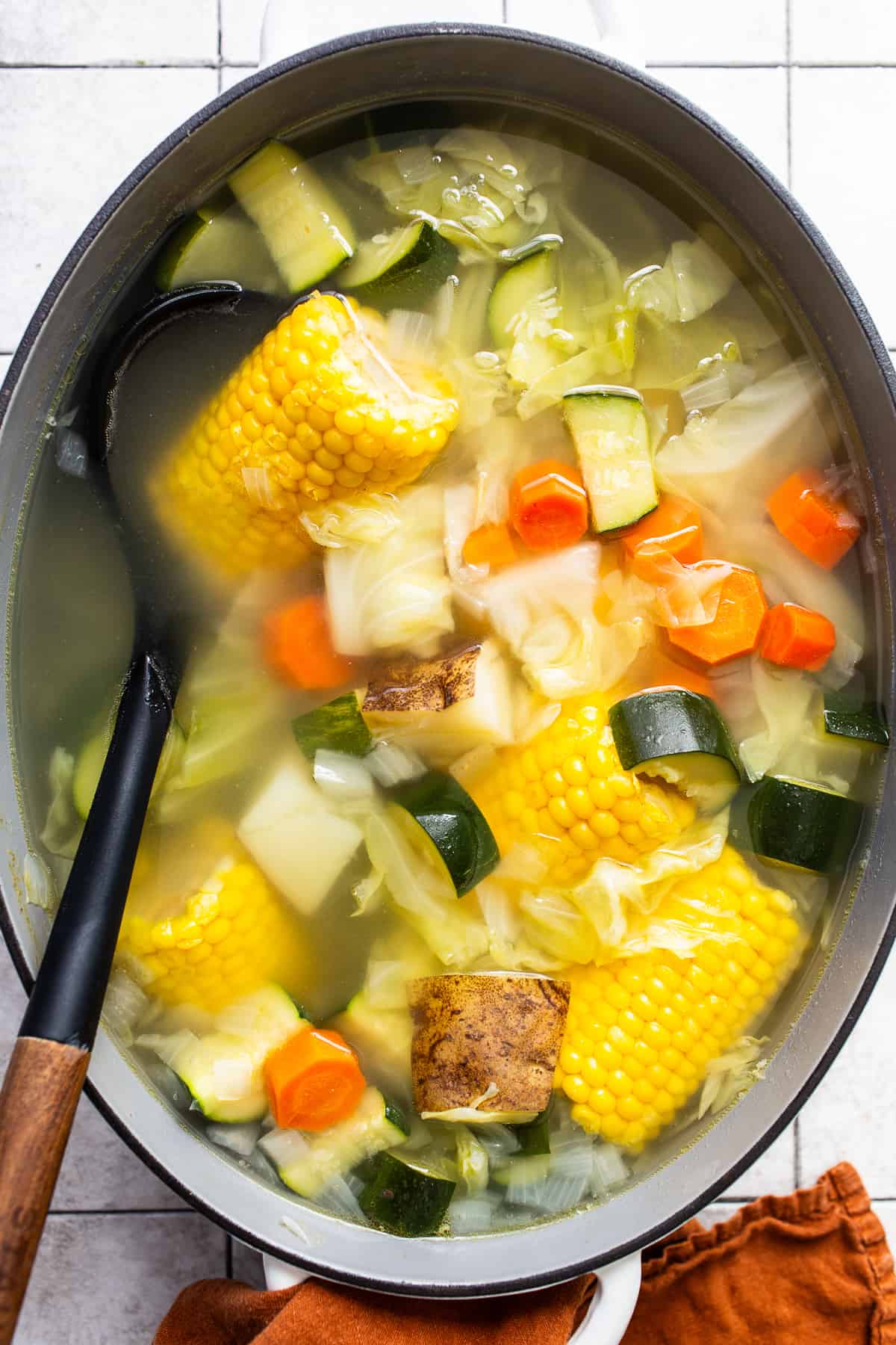Caldo de pollo in a large pot filled with corn, cabbage, chicken, potatoes, zucchini, and more.