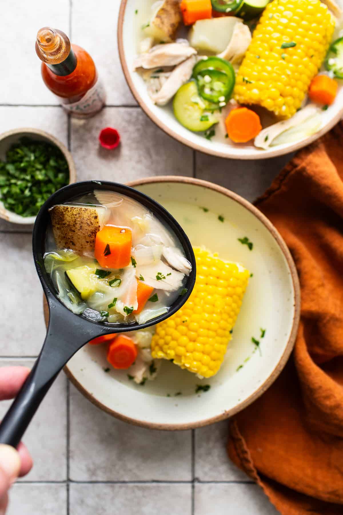 A ladle with caldo de pollo inside.