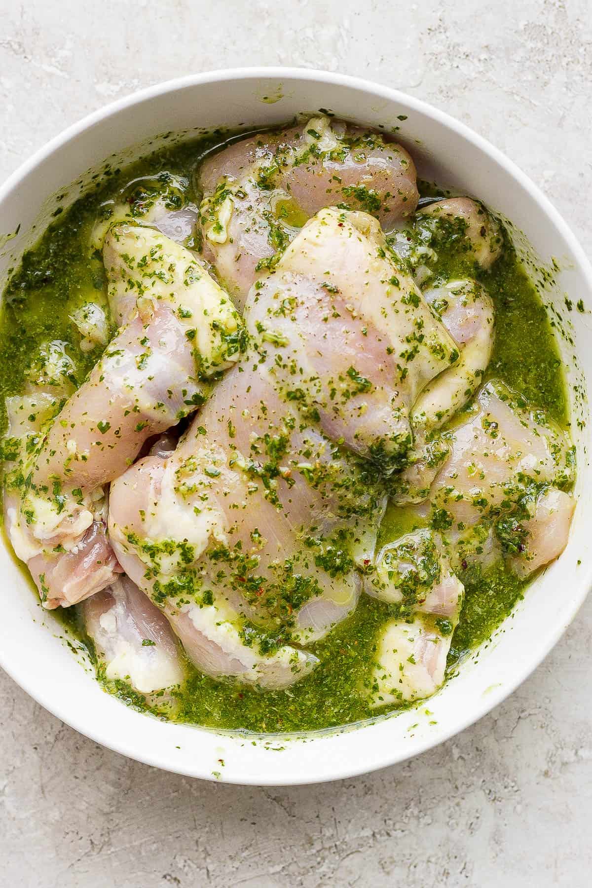 Chimichurri chicken in a bowl marinating in chimichurri sauce.