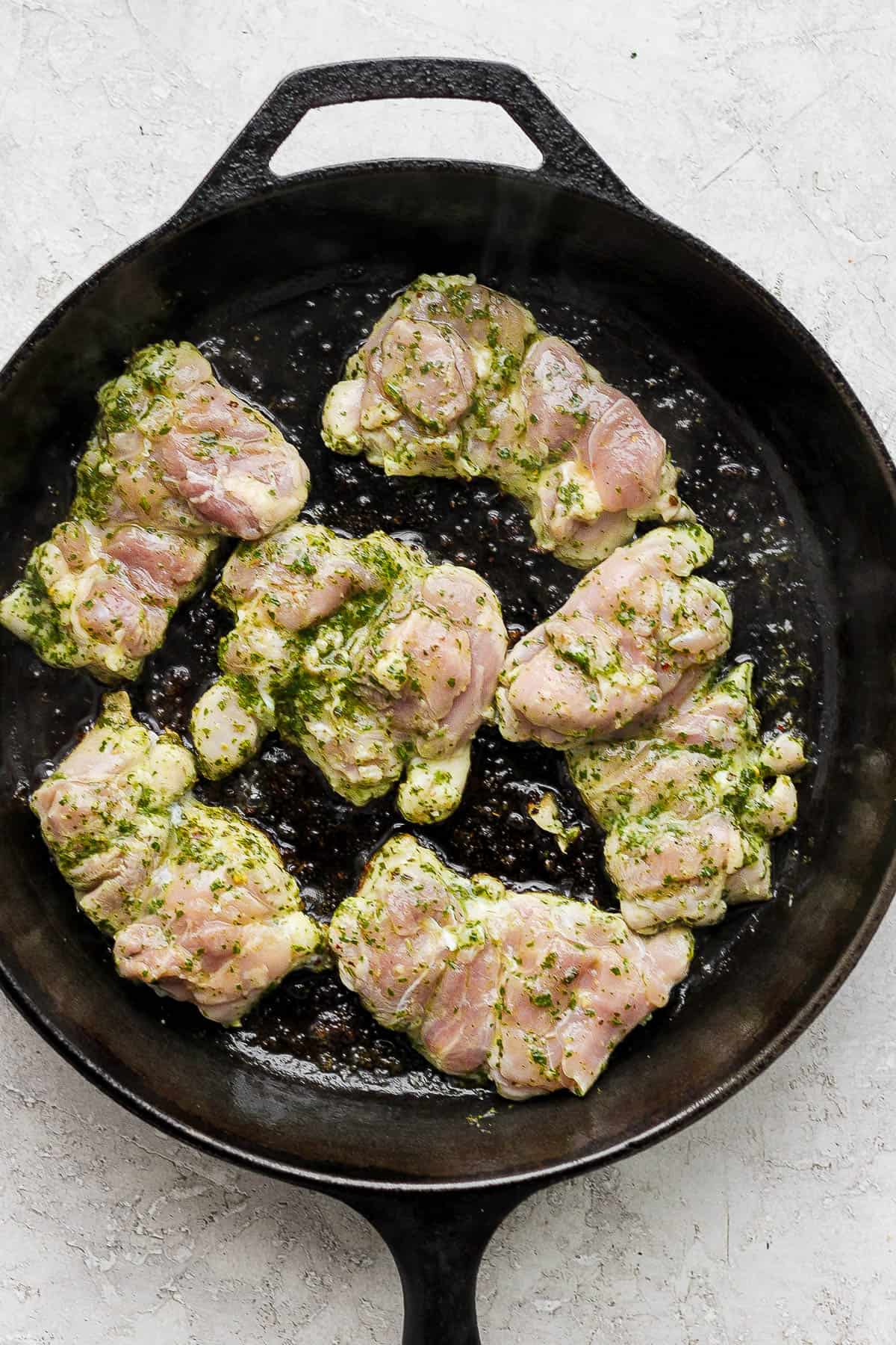 Marinated chimichurri chicken thighs being cooked in a cast iron skillet.