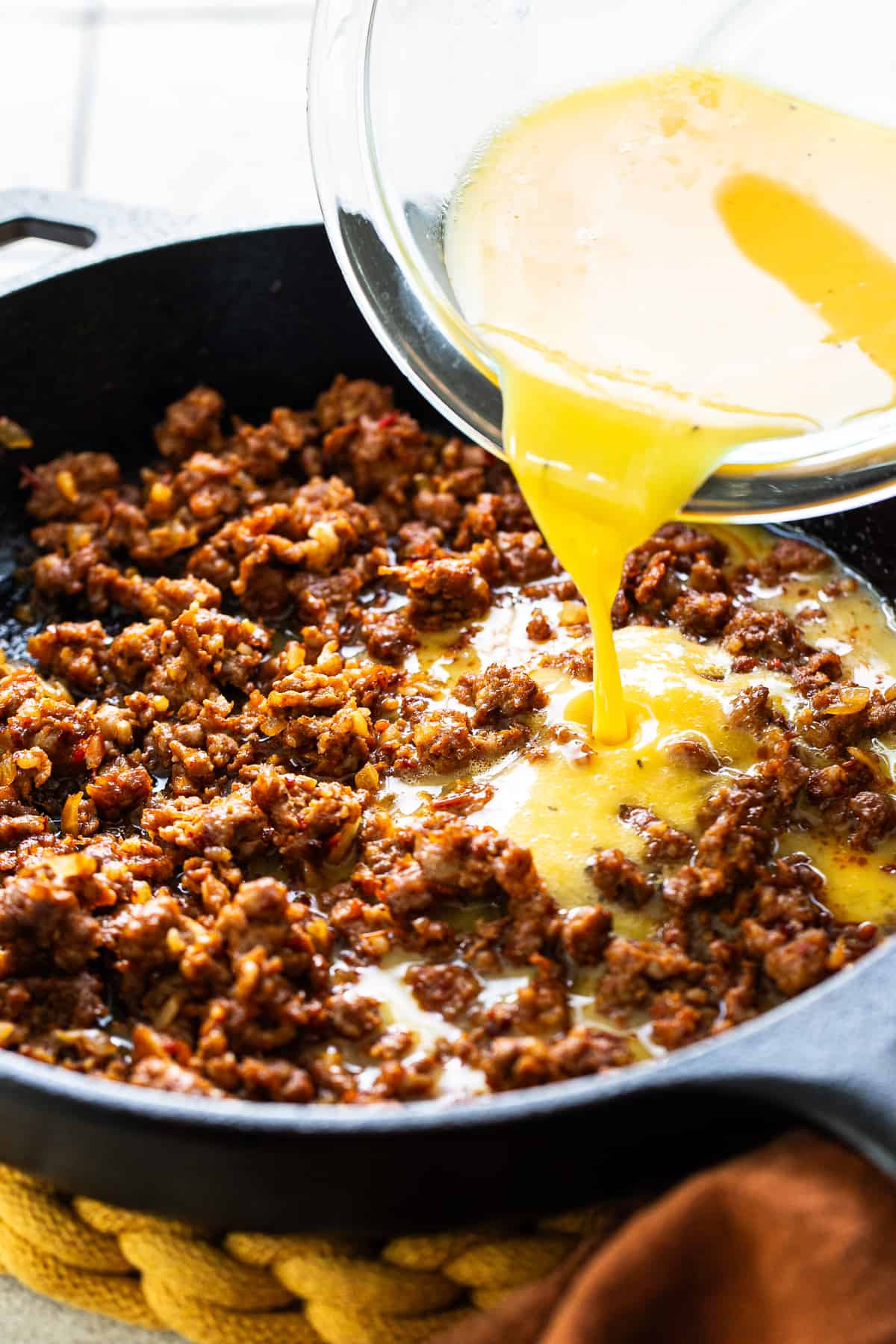 Beaten eggs being poured into a skillet of cooked Mexican chorizo.