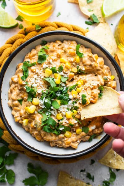 A bowl of Mexican corn dip with a tortilla chip being dipped inside.