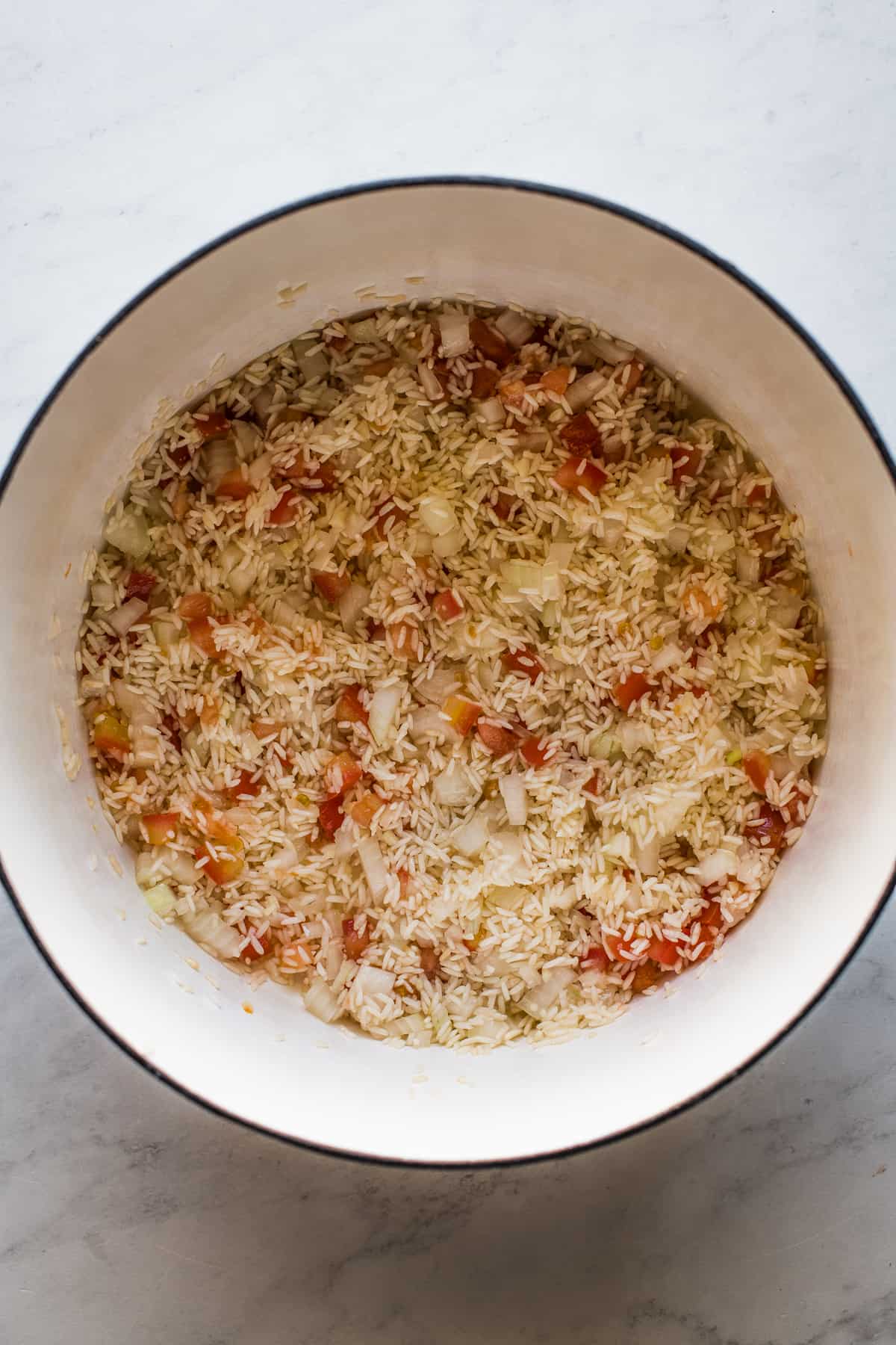 Long grain white rice in a dutch oven with onion and tomato.