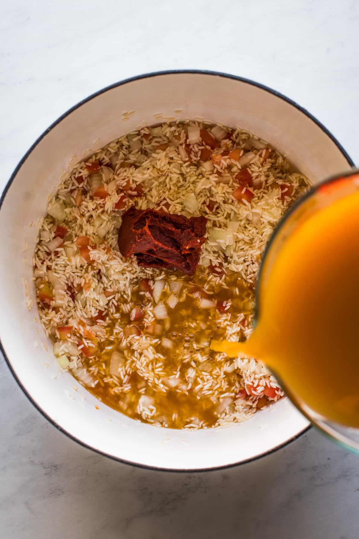 Broth being poured into a pot to make authentic Mexican rice.