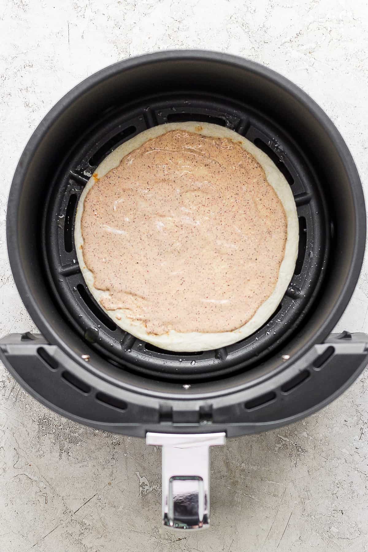 A flour tortilla with a spread of chili lime sauce in an air fryer.