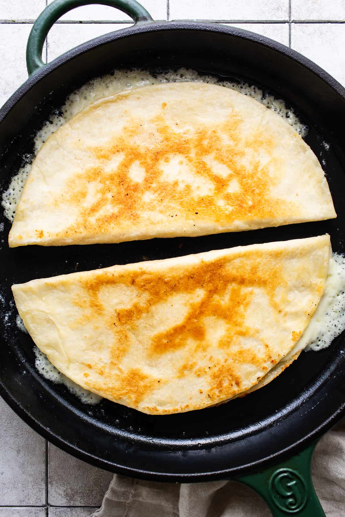 Cheese quesadillas being cooked in a skillet with butter until golden brown and crispy on the outside.