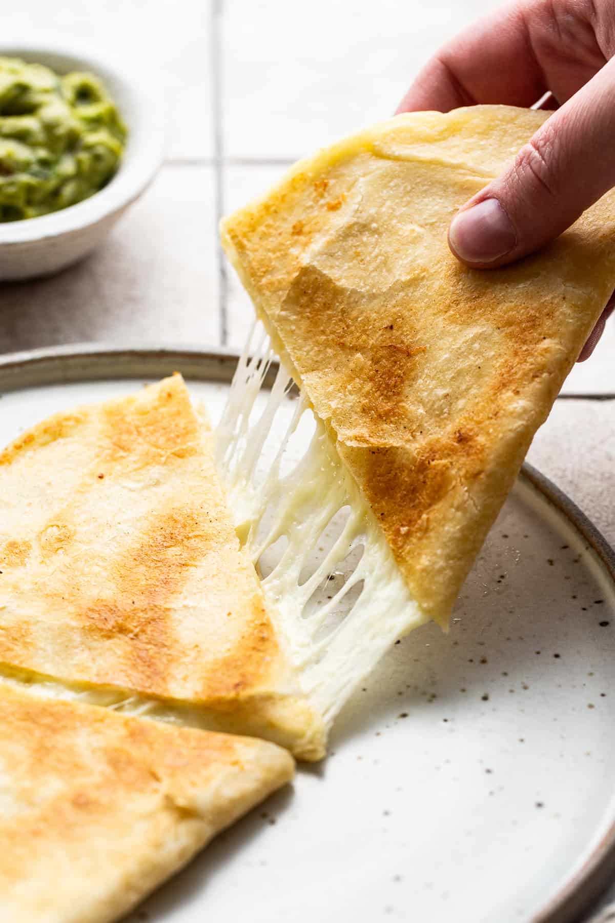 A cheese quesadilla slice being pulled to reveal melted stretchy ooey-gooey cheese.