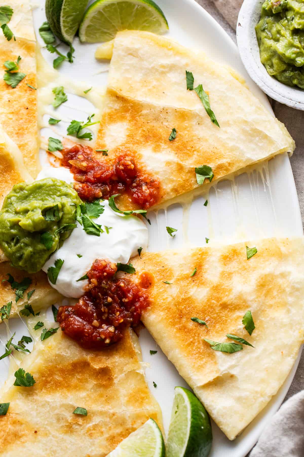 Cheese quesadillas on a plate served with salsa, sour cream, and guacamole.