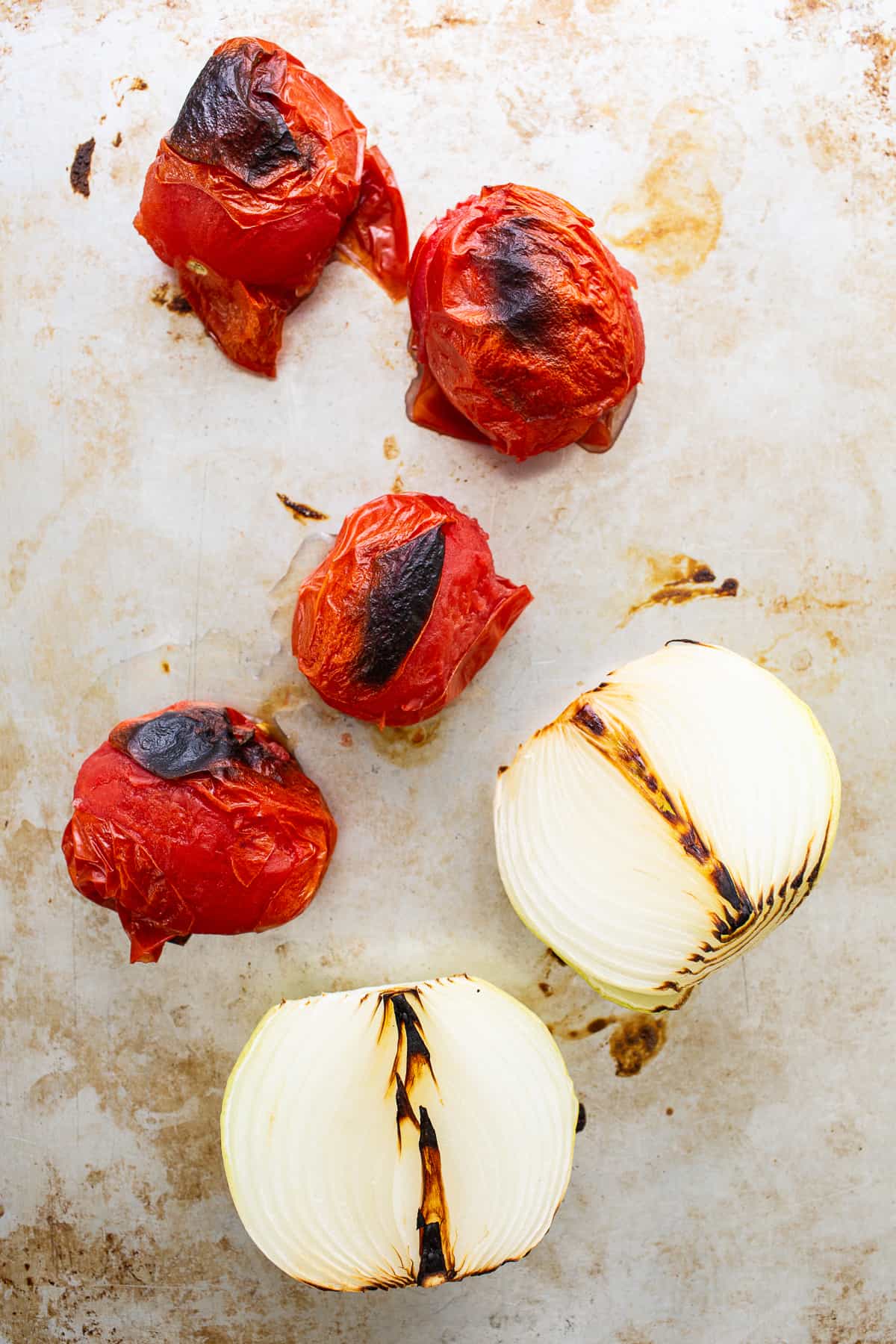 Roasted Roma tomatoes and a white onion on a baking sheet.