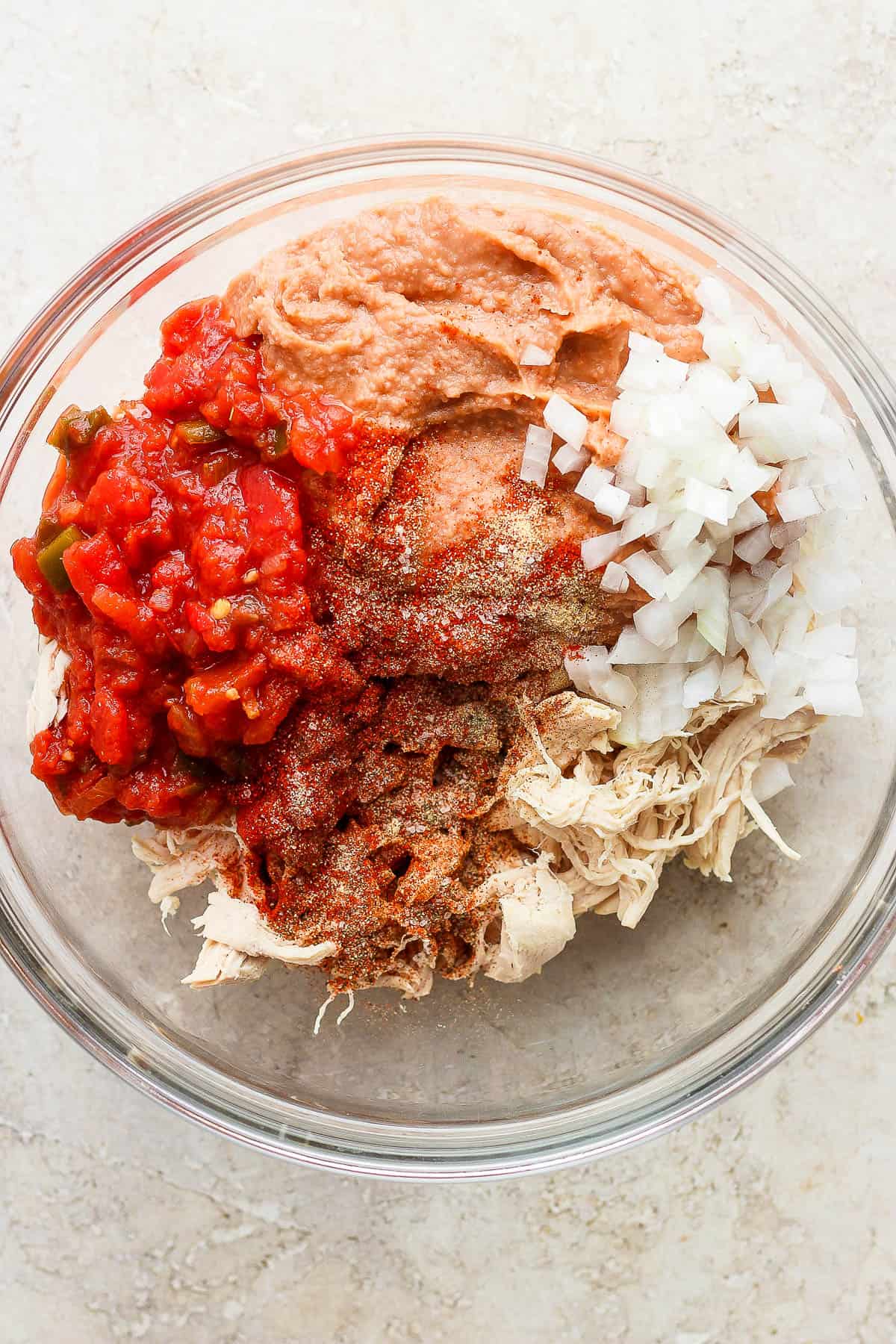 Shredded chicken, refried beans, diced onions, salsa, and seasonings in a large mixing bowl.