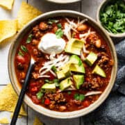 Chorizo chili in a bowl topped with shredded cheese, avocado, sour cream, and served with tortilla chips.