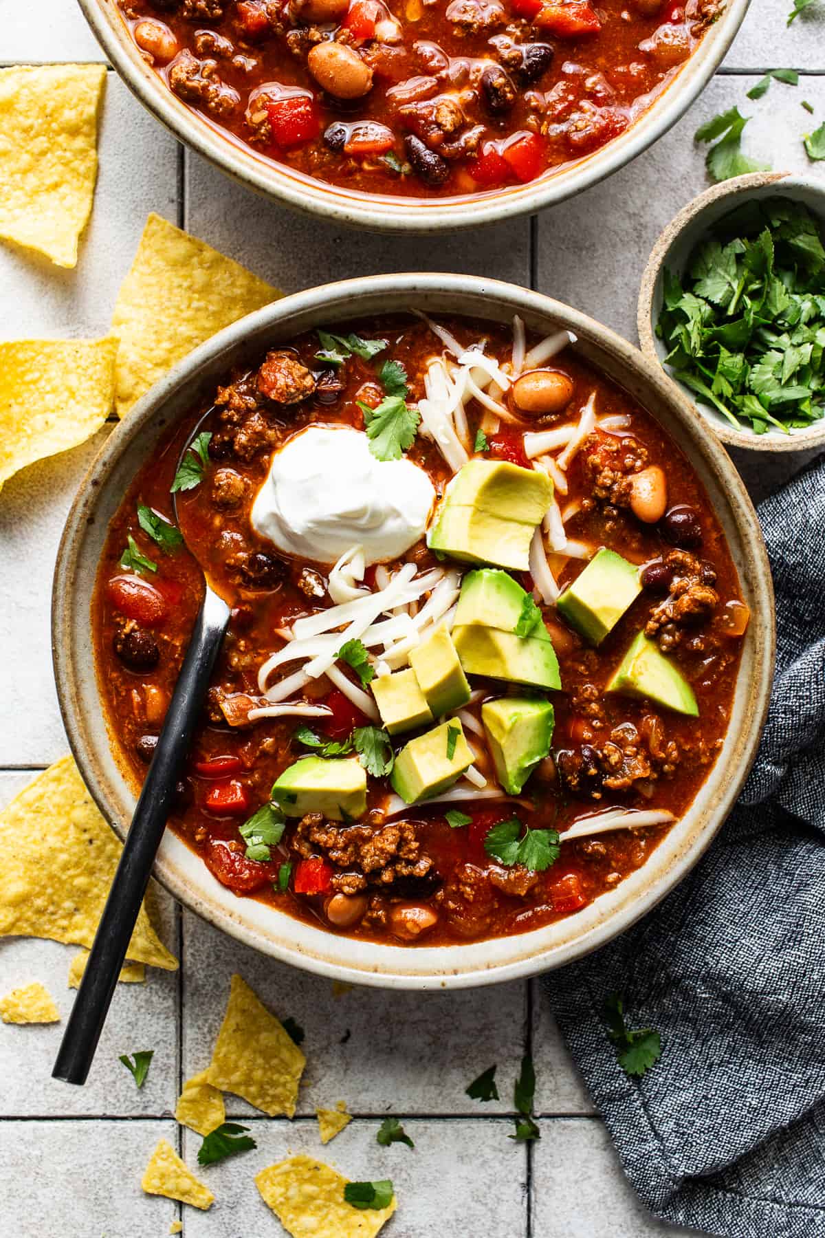 Chorizo chili in a bowl topped with shredded cheese, avocado, sour cream, and served with tortilla chips.