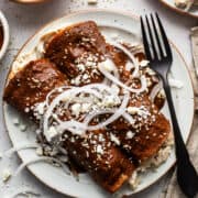 Enmoladas (Chicken Mole Enchiladas) on a plate topped with sesame seeds, queso fresco, and sliced white onions.