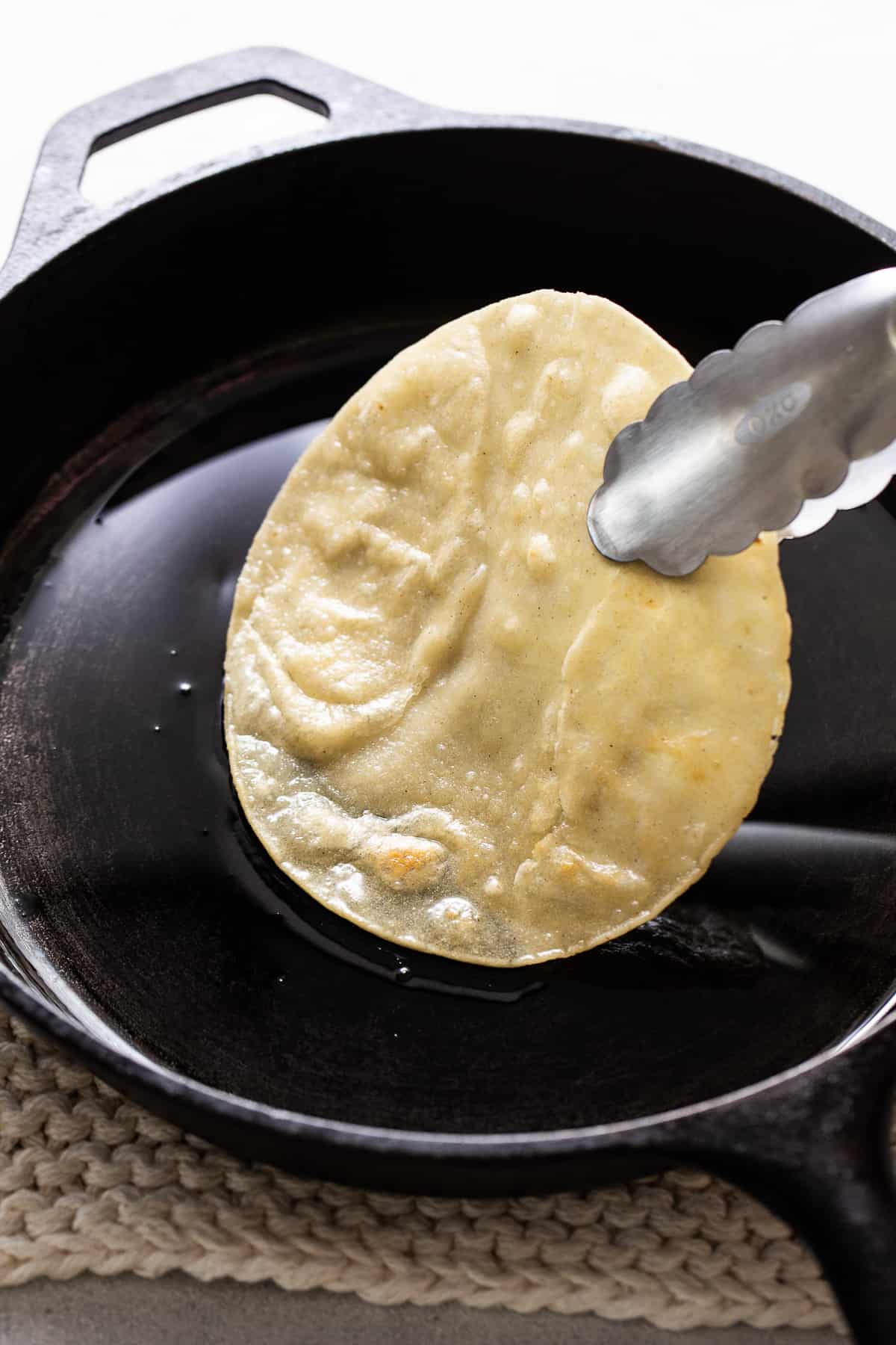 A corn tortilla lightly frying in a pan of oil.