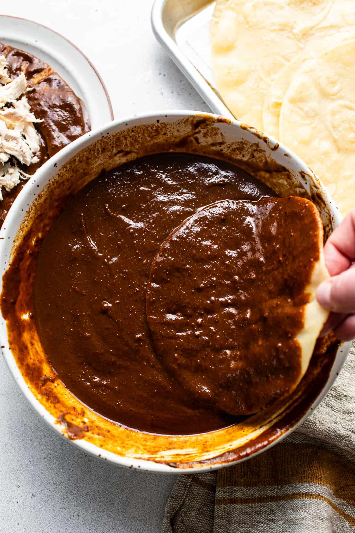 A lightly fried corn tortilla being dipped in mole sauce.