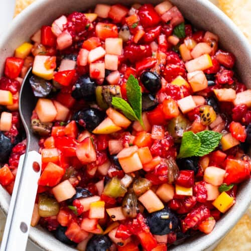 Fruit salsa in a bowl with a spoon and a mint leaf in the middle.