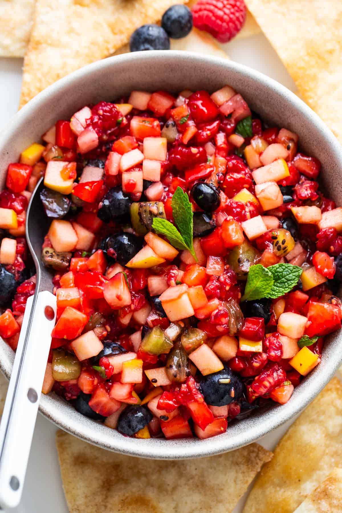 Fruit salsa in a bowl with a spoon and a mint leaf in the middle.