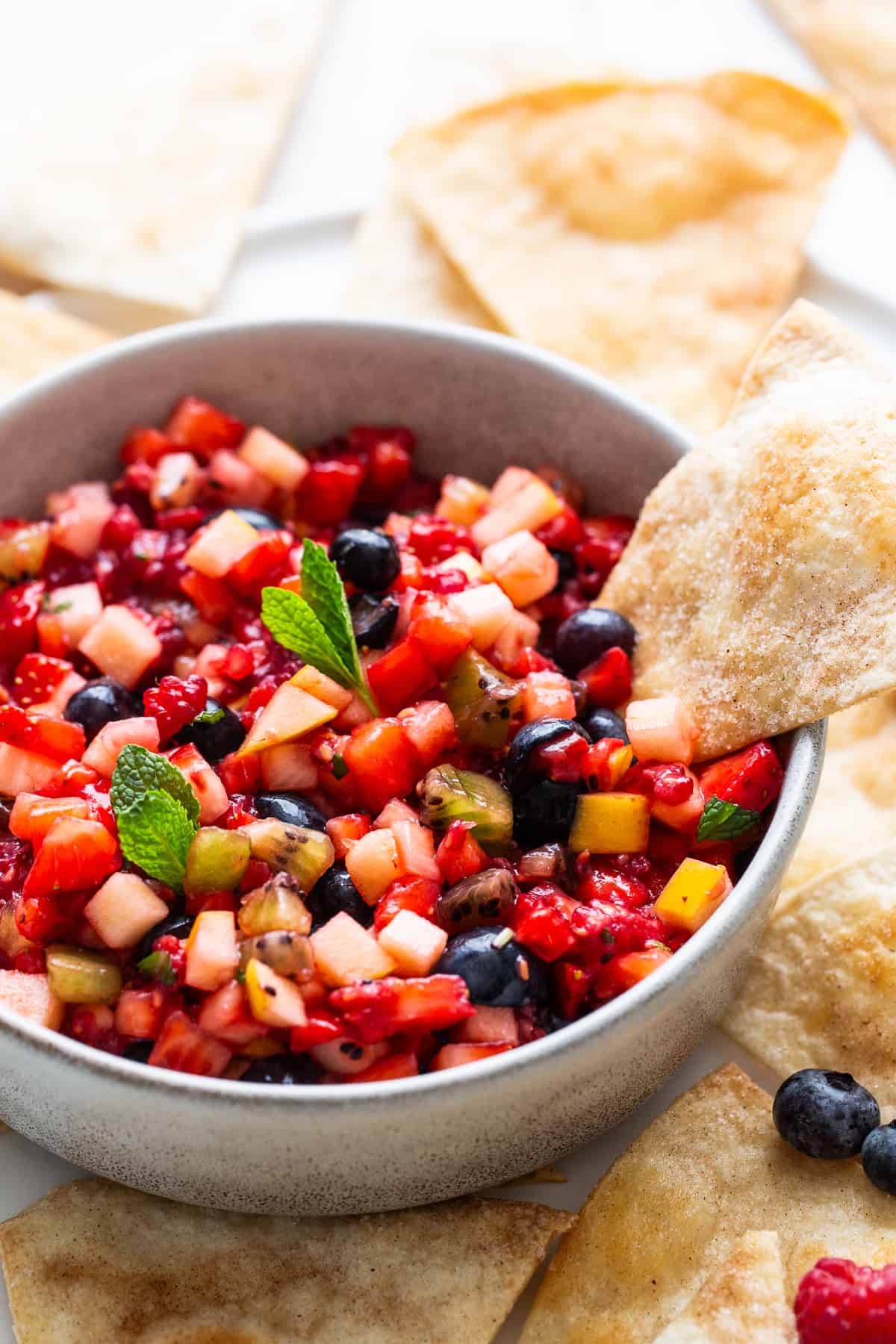 A cinnamon chip scooping some fruit salsa from a serving bowl.