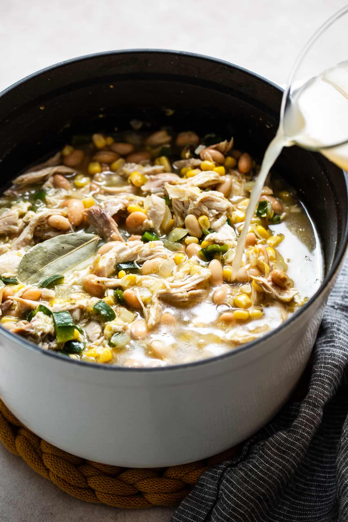 Broth being poured into a pot of green chicken chili.