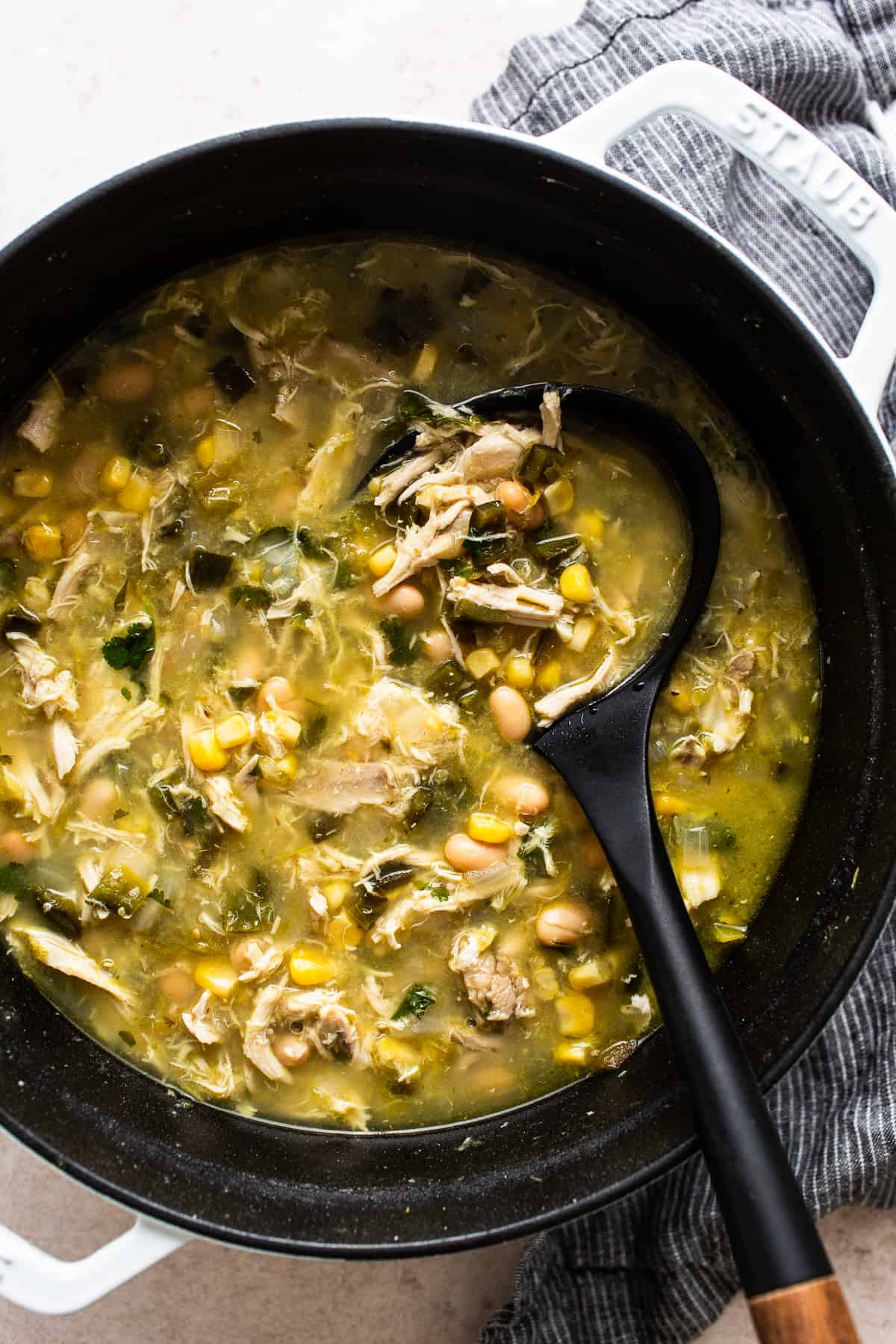 Green chicken chili in a large pot with a ladle.