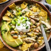 Green chicken chili in a bowl garnished with sour cream, tortilla chips, avocado, cilantro, and green onions.