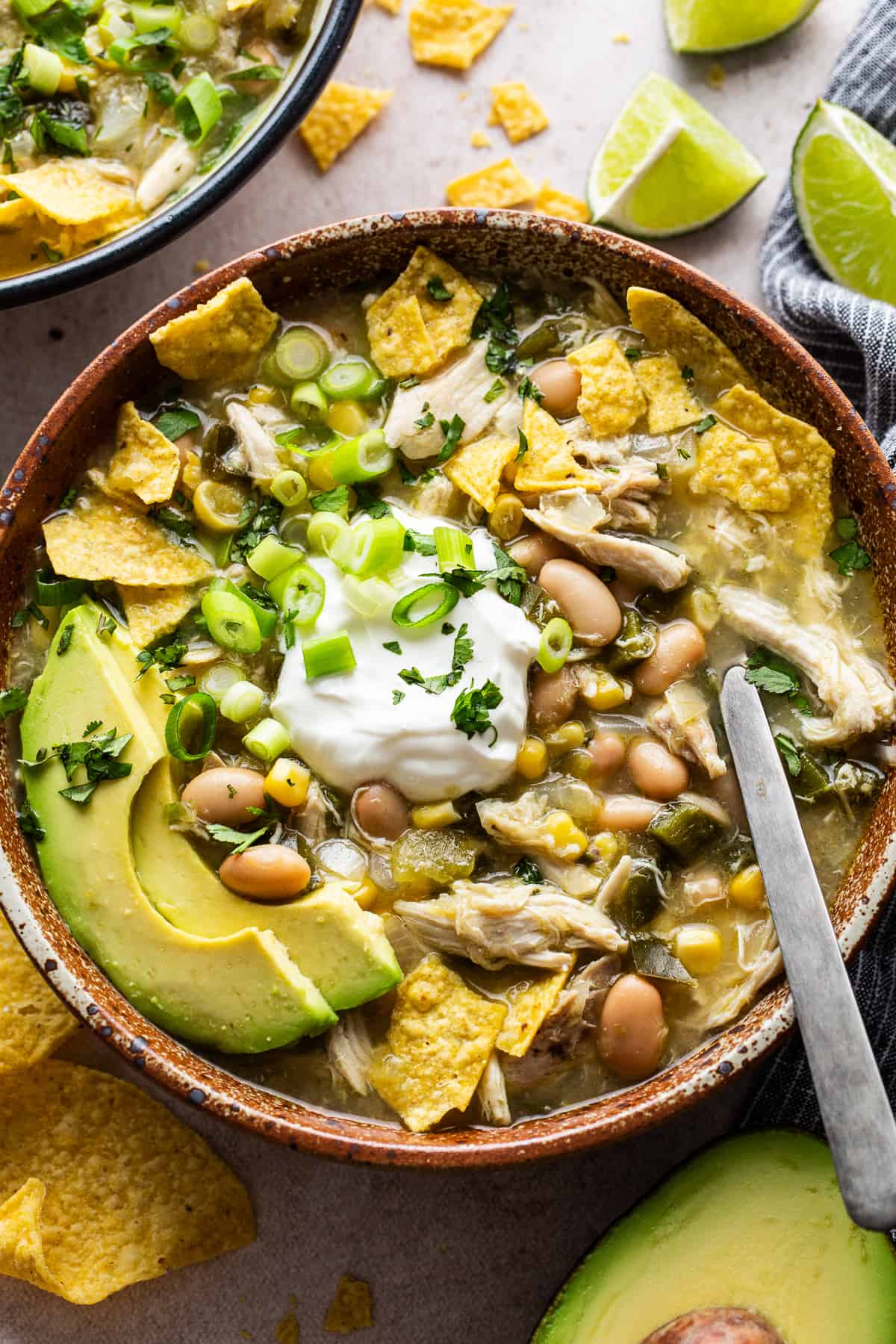 Green chicken chili in a bowl garnished with sour cream, tortilla chips, avocado, cilantro, and green onions.