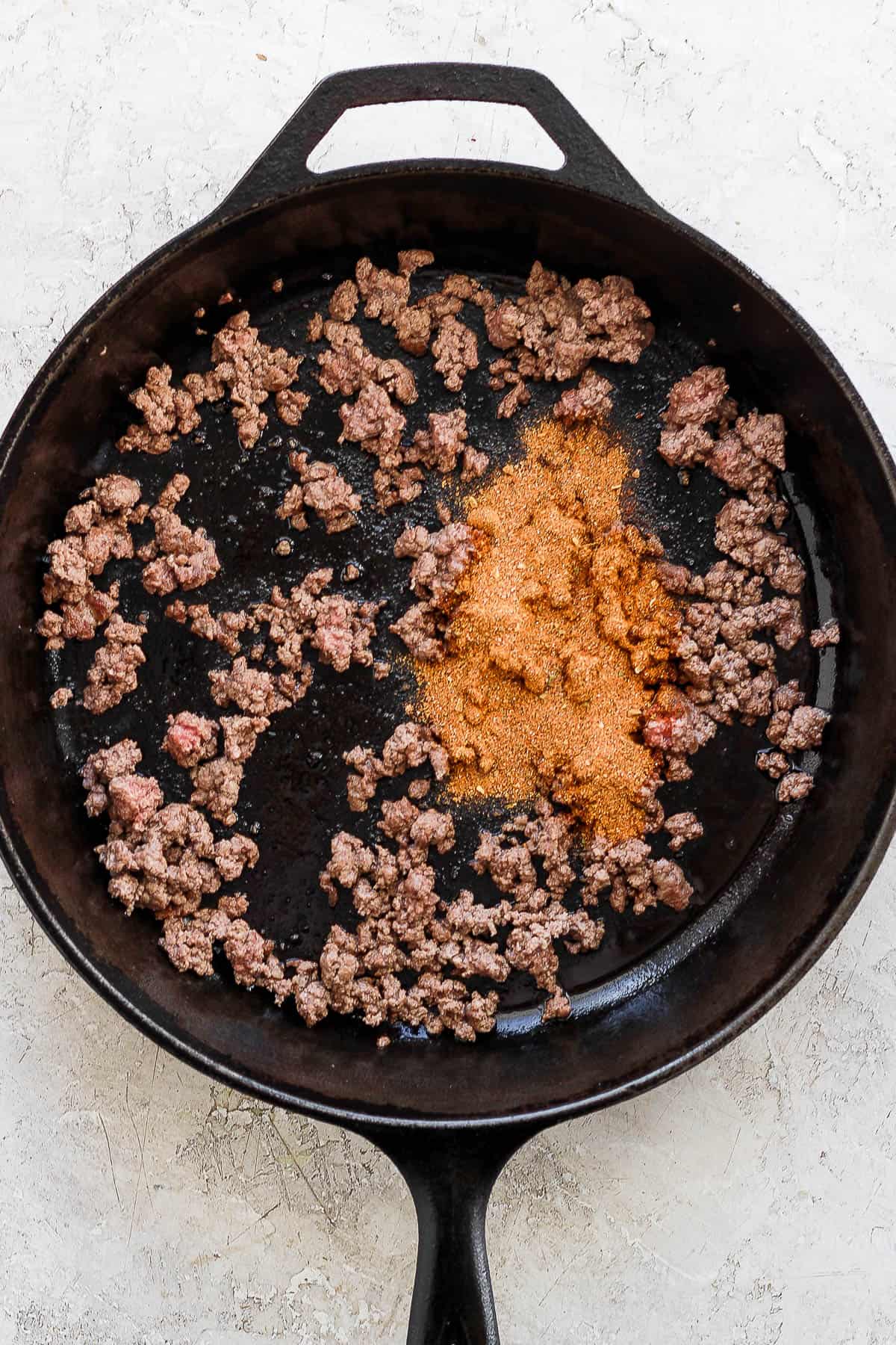 Ground beef and taco seasoning in a cast iron skillet.