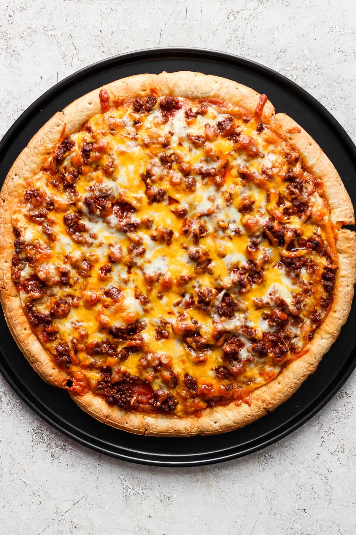 A homemade taco pizza with melted cheese, taco meat, salsa, and refried beans.