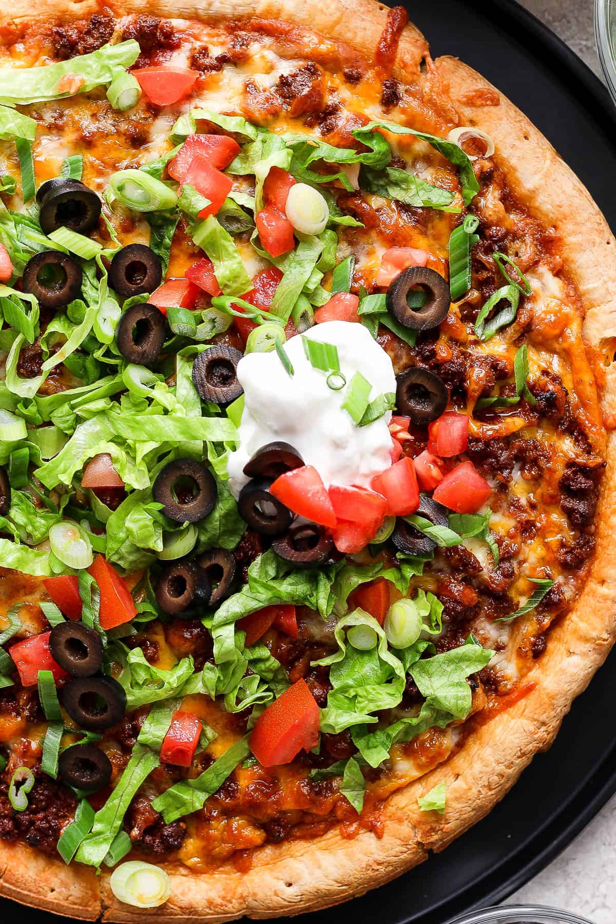 Easy taco pizza topped with sour cream, shredded lettuce, diced tomatoes, and other taco toppings.