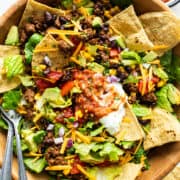 A big bowl of taco salad with ground beef, cheese, lettuce, beans, sour cream, salsa, and tortilla chips.