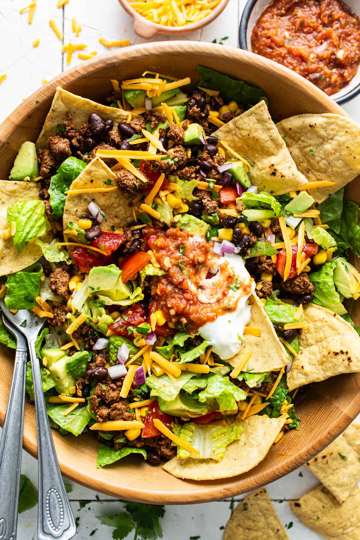 A big bowl of taco salad with ground beef, cheese, lettuce, beans, sour cream, salsa, and tortilla chips.