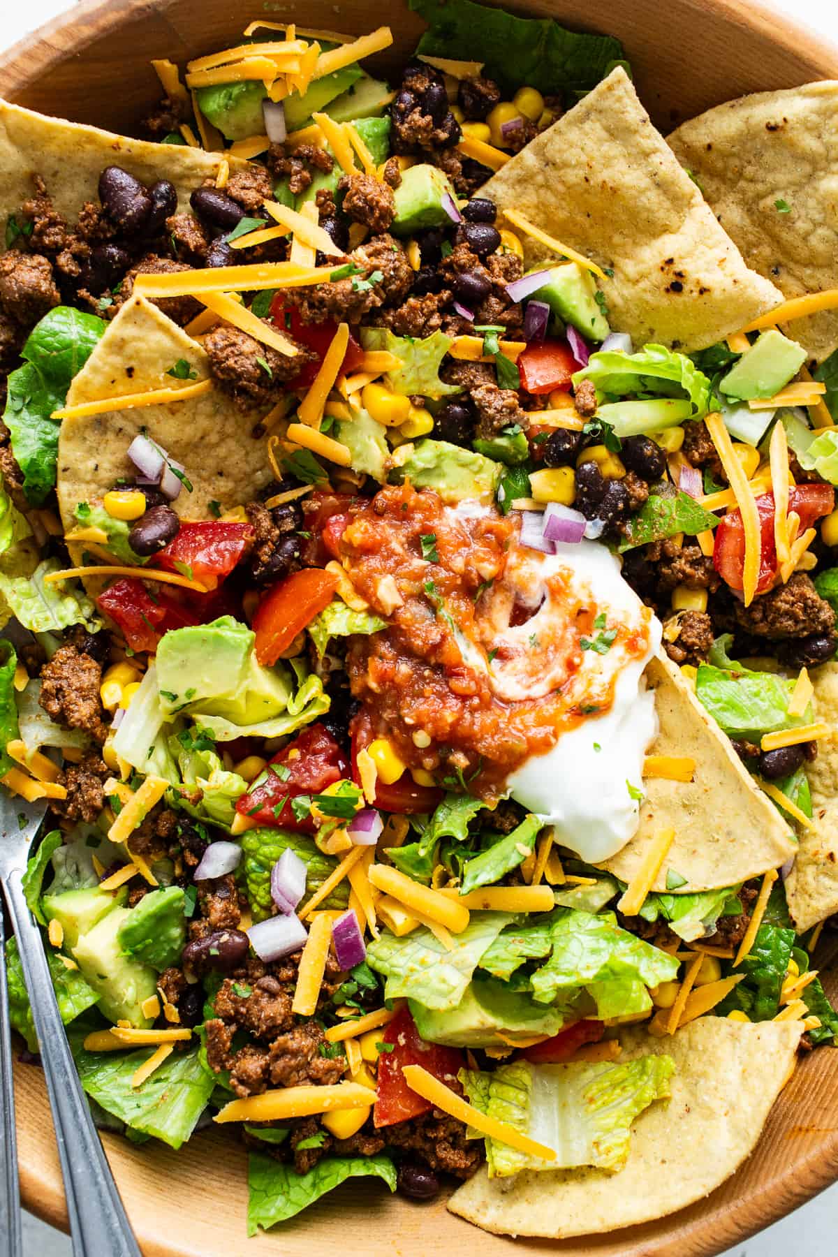 A taco salad bowl garnished with shredded cheddar cheese, sour cream, and chunky salsa.