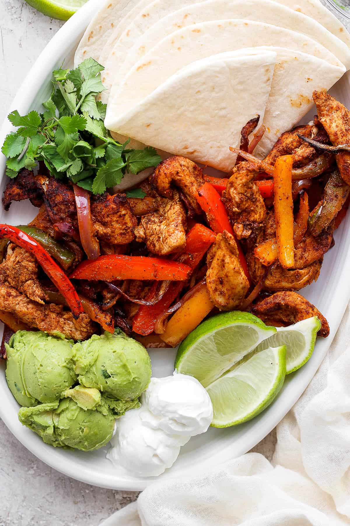 Plated air fryer chicken fajitas with tortillas, limes, sour cream, guacamole, and cilantro. 