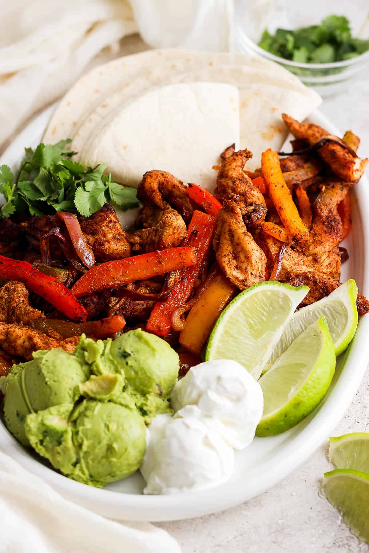 Plated air fryer chicken fajitas with limes, guacamole, and tortillas. 