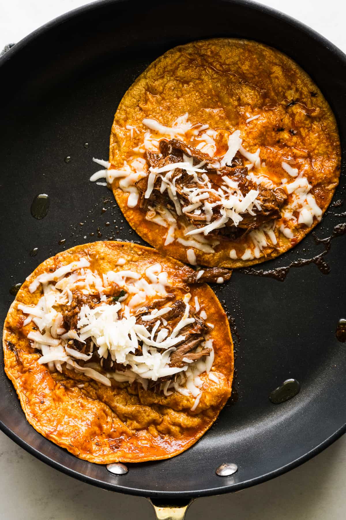 Birria tacos frying in a skillet.