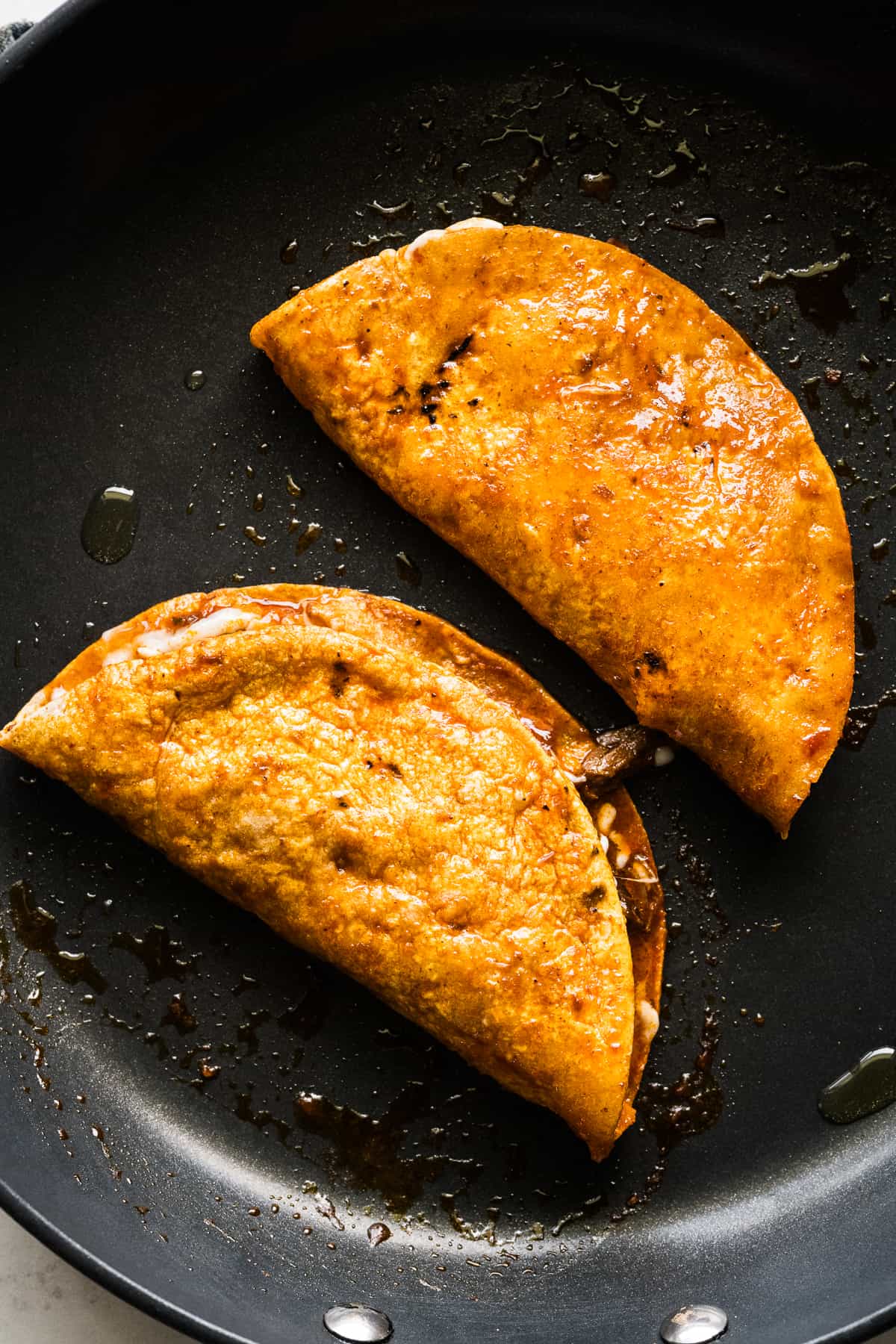 Birria tacos folded over and crisping up in a skillet.