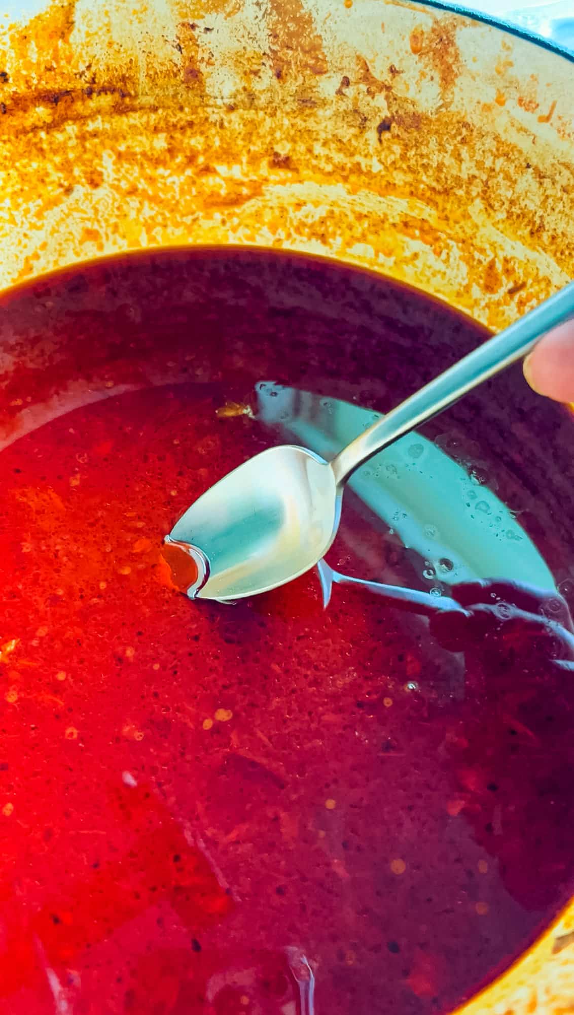 A spoon dipped in the top layer of fat of a pot of birria for making tacos.