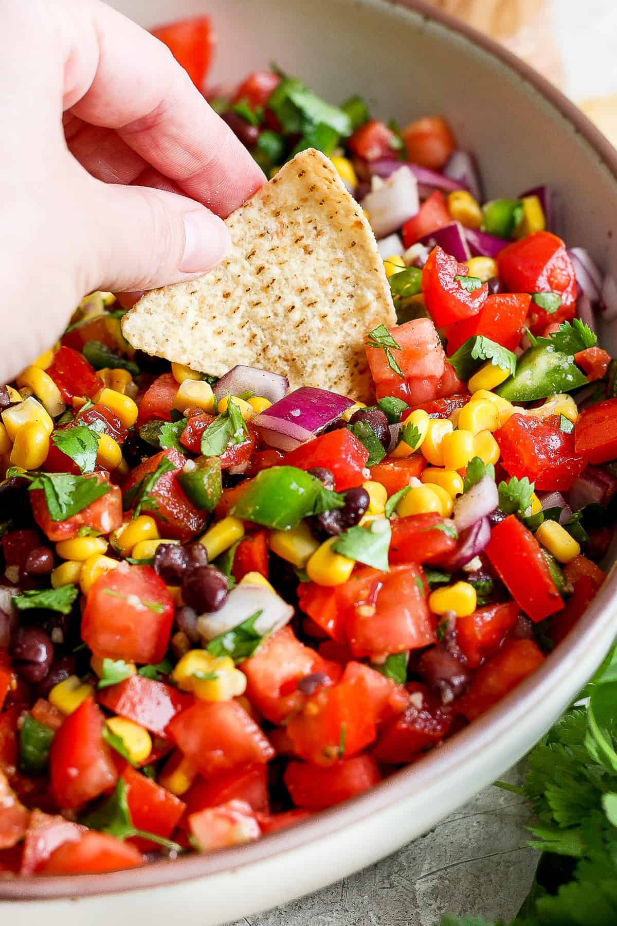 A tortilla chip being dipped into a bowl of black bean and corn salsa.